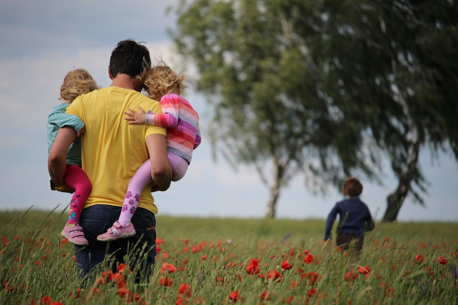 Berufsunfaehigkeit-vs-Dread-Disease-Vergleich Rückenansicht von junger Familie auf Blumenwiese